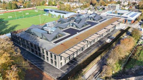The new Peebles High School building viewed from above with pointy sections to its roof and sports pitches in the background