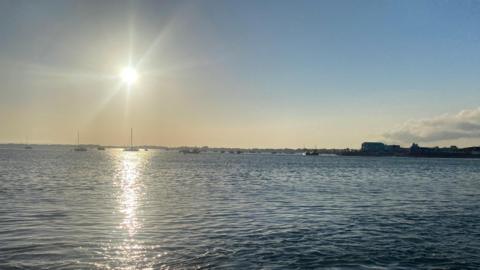 The sun shines down on the sea leaving a dappled effect through the picture towards the horizon where boats pepper the surface