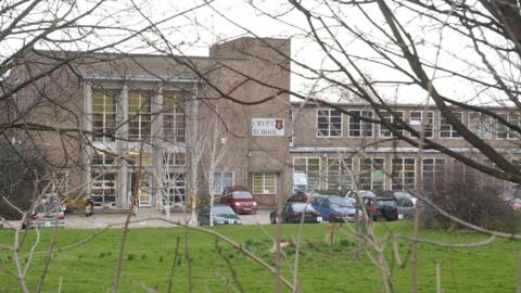 Wide shot of the outside of The Crypt School in Gloucester showing the front of the school, cars in the car park and a lawn.