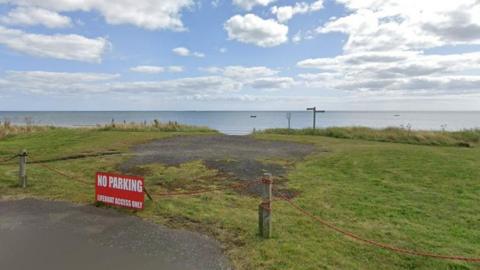 Grassy bank with beach and sea in background. A sign reads no parking - lifeboat access only.