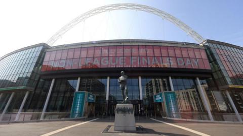The Bobby Moore statue outside the front of Wembley. The arch is towering above the stadium and the sign reads "Welcome to Non-League Finals Day".