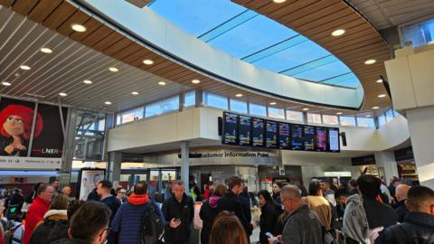 Crowds of passengers looking at boards in a train station.