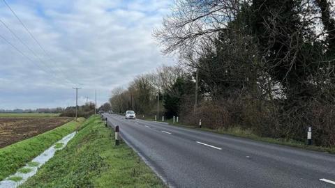 View of Pullover Road, which is where the man's body was found. It is a two-lane road with trees overhanging on one side, and a ditch leading to farmland on the other.