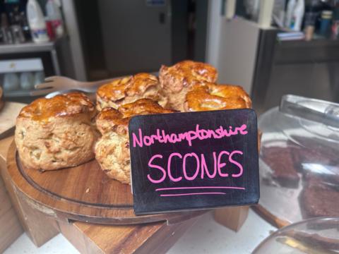 Four freshly baked scones on a plate. There is a hand-written sign on a slate saying "Northamptonshire Scones"