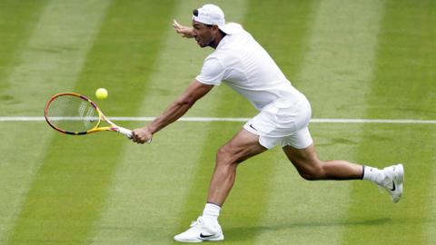 Rafael Nadal wearing white sports clothes playing tennis on a grass court at Wimbledon