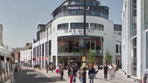 A stock image of people walking down Cheltenham High Street near the Brewery Quarter on a sunny day