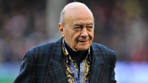 File photo dated 12-01-2013 of Fulham owner Mohamed Al-Fayed. He is wearing a paisley shirt underneath a navy tartan blazer and is looking towards his left. He is bald, and is shaven.