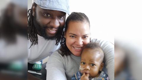 A man and a woman with a baby smiling.