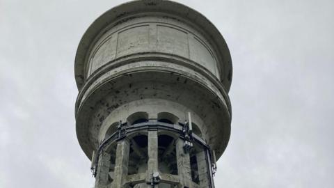 The top of a concrete water tower dating from the 1920s with an array of telecommunications equipment on it