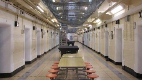 HMP Leeds interior, with tables and stools in the foreground, and a staircase in the background. Rows of cells are on either side.