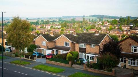 A general view of houses in the Allestree area of Derby. It is a suburban street with brick-built houses facing on to a tree-lined street, behind which more houses and trees are visible.