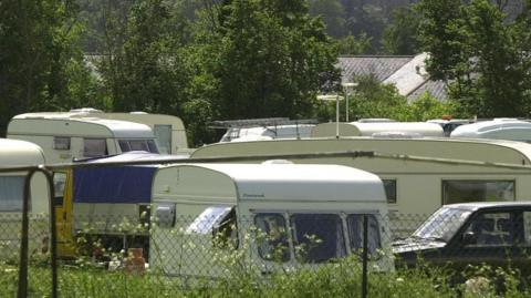 Several caravans parked up behind a black mesh fence.