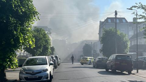 Police tape with smoky skyline beyond residential street with parked cars