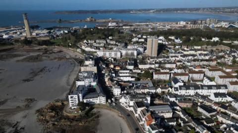 A drone shot of Jersey. There are a multitude of different buildings, and the tide is out, leaving the muddy seabed beneath.