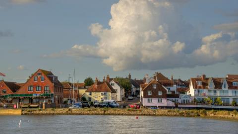 Photo shows Emsworth waterside with colourful cottages and a yacht and the water in front