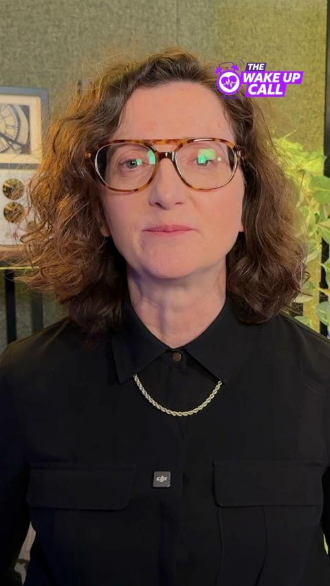 A woman wearing a black shirt is looking towards the camera. She is sitting inside. A purple logo which says The Wake Up Call is in the top right corner of the screen. 