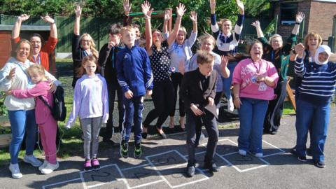 Children and staff at the Elmley Dray School in Minster-on-Sea, Sheerness, Kent jump up with joy with their hands in the air. They all look very happy. 