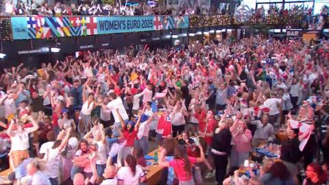  A large crowd in red and white shirts stands and cheers in celebration at Boxpark in Wembley.