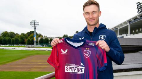 Chris Benjamin holds up at Kent Spitfires shirt at Canterbury