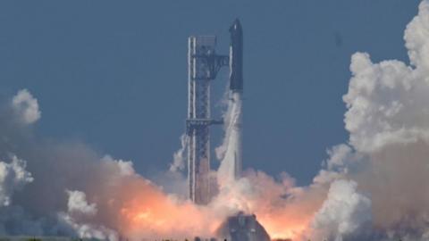 A black SpaceX Super Heavy booster carrying the Starship spacecraft lifts off.