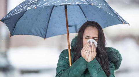 Woman sneezing under an umbrella on a cold, wet day