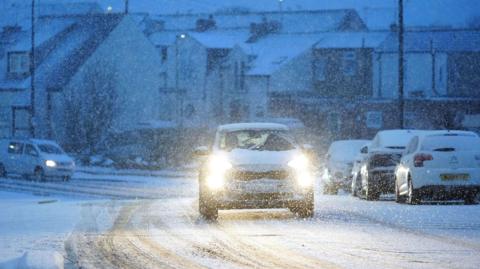 A car with headlights on driving in dim snowy conditions in Cullercoats on North Tyneside.