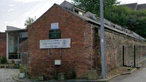 A single storey brick building with a white sign with blue writing which reads Williamson Tunnels Heritage Centre