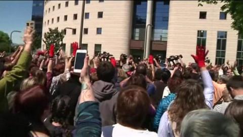 Protesters - some raising a single red-gloved hand - chant in numbers outside the court