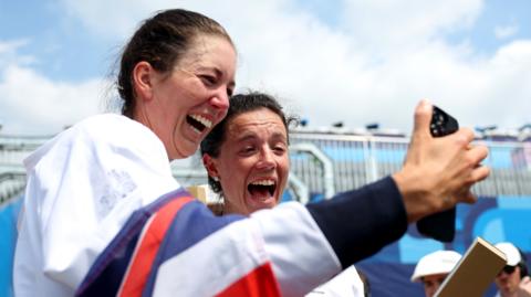 Gold medalists Emily Craig and Imogen Grant of Team Great Britain talk with their family with mobile phone after the Rowing Lightweight Women's Double Sculls medal ceremony on day seven of the Olympic Games Paris 2024 at Vaires-Sur-Marne Nautical Stadium on August 02, 2024 in Paris, France.