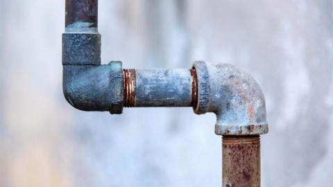A stock image of a metal water pipe in front of a blurred background. 