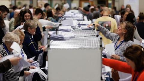 Dozens of people counting ballot papers in an election count centre.