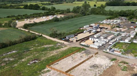 A complex of fields with mobile homes and caravans. An additional field has been occupied by caravans on hard standing, with an untouched green field in between the existing site and the new site. 