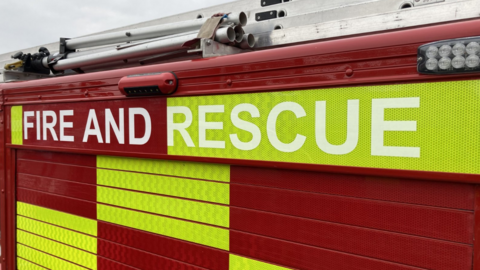 The side of a fire engine with red and green/yellow rectangles in a pattern and "fire and rescue" written on the side.