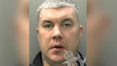 Mugshot photo of Liam Collins, 36. He has short silver hair, green eyes and looks directly at the camera. There is a Gwent Police logo in the bottom right of the image.