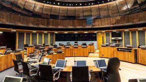 An empty Senedd chamber, with desks arranged in circular formations with computers on them. 