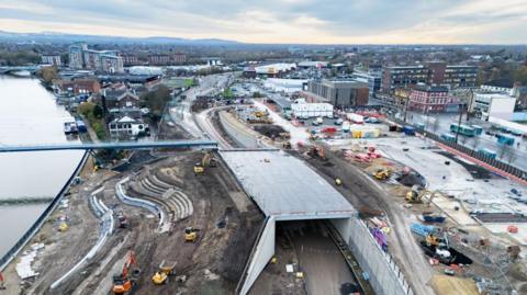Construction work along the waterfront area of Stockton. A number of diggers and similar vehicles are on the site. To the left of the image, curved granite steps are being put in place to create a terraced area near where a footbridge spans the River Tees.