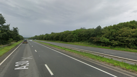 A google street view image of the A30 near Liftondown heading westbound. It is a dual carriageway with green bushes lining either side of the road. The sky is grey. 