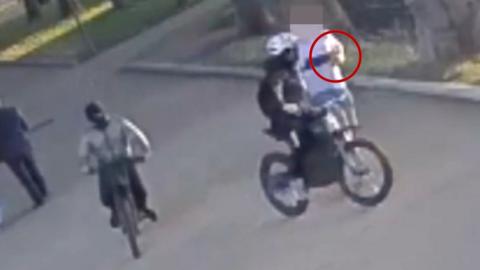 Person on a bike, with their face covered, reaches out to snatch a phone from a pedestrian.  