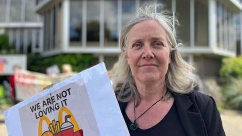 Emma Russell wearing a black blazer and holding a sign saying 'we are not loving it'