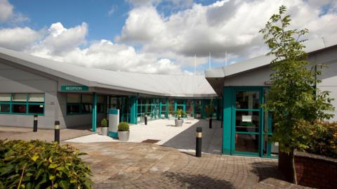 A grey one-storey building with green windows and door frames