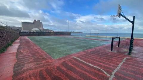 An unkept basketball court next to the sea.