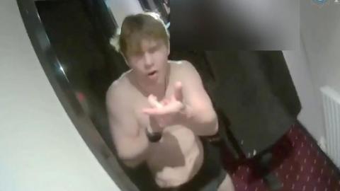A screen shot of a young man wearing a pair of black underpants miming shooting a gun.  