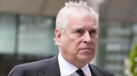 A picture of Andrew Mountbatten-Windsor, who has white hair and is wearing a black jacket, black tie and white shirt.