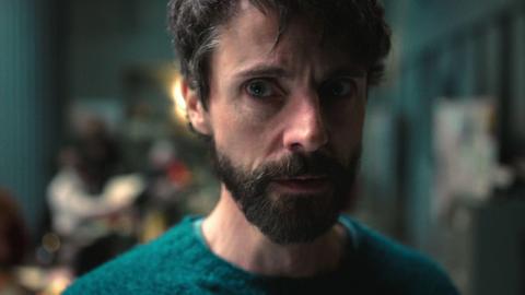 Close up of a man wearing a green jumper staring off to the right of the camera.
