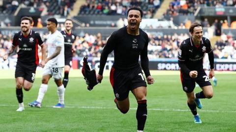Cameron Archer (centre) runs with his fists clenched and his shirt in his right hand after scoring for Southampton