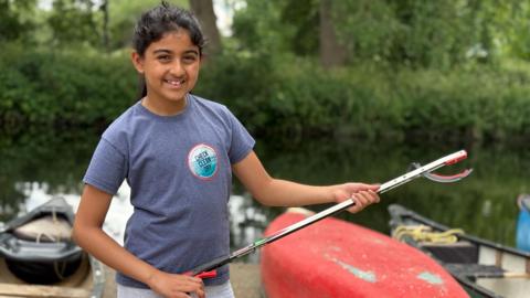 A 10-year-old girl in a purple t-shirt poses with her litter grabber.