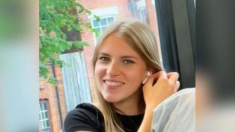 Sophie Goode is pictured smiling wearing a black top and grey trousers