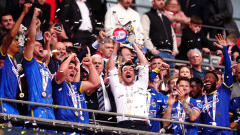 AFC Wimbledon manager Johnnie Jackson (centre) lifts the trophy with players following victory in the Sky Bet League Two play off final