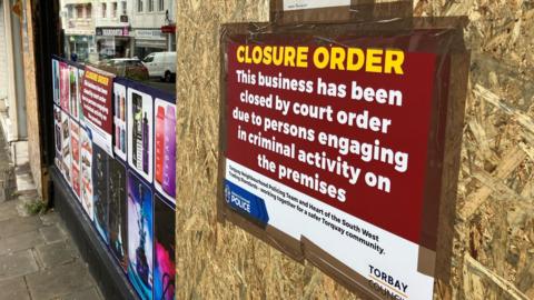 The outside of a boarded up shop in Torbay with a big closure order poster displayed. 