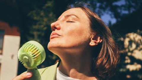 A woman cooling herself with a handheld fan.